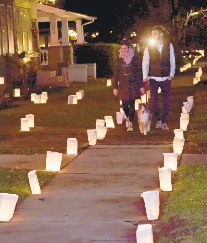  ?? PHOTOS BY AMY SHORTELL/THE MORNING CALL ?? Ben and Jennie Richter walk their dog, Lilly, on West Market Street in Bethlehem on Saturday night during the 21st annual Luminaria Night. The money raised from the sale of candles, sand and white paper benefits New Bethany Ministries.