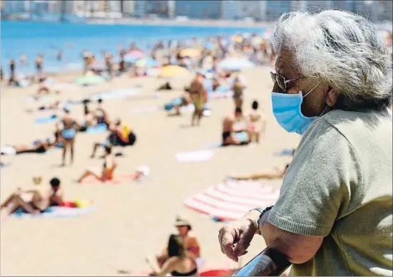  ?? BORJA SUAREZ / REUTERS ?? Una mujer protegida con una mascarilla observa a los bañistas de Las Canteras, una de las playas de Las Palmas de Gran Canaria