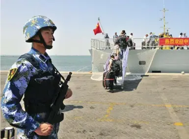  ?? CHINA STRINGER NETWORK/REUTERS ?? A Chinese navy soldier stands guard as Chinese citizens board the ship Linyi at a port across the Gulf of Aden from Djibouti.