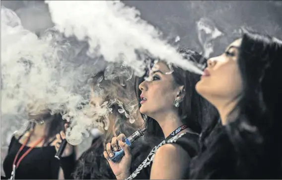  ?? Photos: Mohd Rasfan/AFP and Regis Duvignau/Reuters ?? No smoke, no fire: Promoters smoke electronic cigarettes at a Vape Fair in Kuala Lumpur. E-cigarettes, which use vials of flavoured nicotine (left), are said by some medical authoritie­s to help smokers quit. But others say there is not enough evidence...