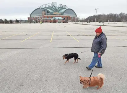  ?? MIKE DE SISTI/MILWAUKEE JOURNAL SENTINEL ?? Tom Giesfeldt of Milwaukee walks his dogs in an empty Miller Park parking lot on what would have been the Milwaukee Brewers’ opening day game against the Chicago Cubs Thursday. The game was postponed due to the coronaviru­s pandemic.