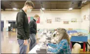  ?? (NWA Democrat-Gazette/Lynn Kutter) ?? Prairie Grove High seniors Blake Gardner (left) and Knox Laird prepare to receive their ballots for the Feb. 8 special election in Prairie Grove. Election official Peggy Hatfield is assisting Gardner. City voters approved all nine questions on the election ballot.