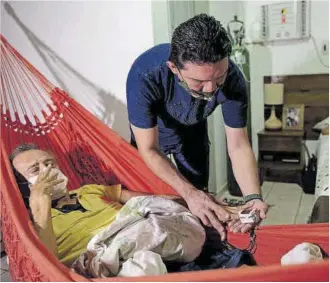  ?? Michael Dantas / AFP ?? El médico Marcos Fonseca asiste a su padre, enfermo de covid, en su casa de Manaos.