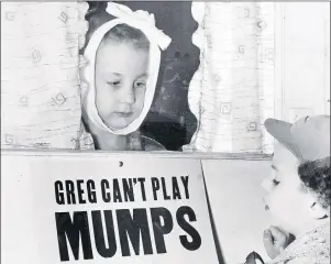  ?? CP PHOTO ?? In a 1957 photo Jon Douglas, 6 visits his friend, Greg Cox, standing behind a sign warning he has mumps, on the door of his home in Altamont, Ill. Fifty years ago, mumps was once a childhood rite of passage of puffy cheeks and swollen jaws. That all...