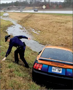  ?? Arkansas Democrat-Gazette/RICK McFARLAND ?? State police officer J. Berry catches himself Saturday while slipping on the wet grass after he walked down an embankment to check on an abandoned vehicle that had slid off Interstate 40 near Burns Park in North Little Rock. The male driver reportedly...