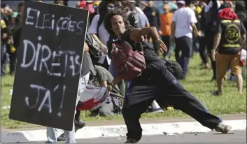  ??  ?? Demonstrat­ors clash with police next to a sign used as a shield with text written in Portuguese that reads “Direct Elections Now” during an anti-government protest in Brasilia, Brazil on Wednesday. Brazil’s president ordered federal troops to restore order in the country’s capital following the evacuation of some ministries during clashes between police and protesters who are seeking the leader’s ouster. AP PHOTO/ERALDO PERES