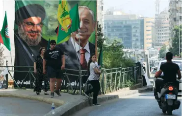  ?? (Jamal Saidi/Reuters) ?? PEOPLE WALK PAST a campaign banner showing Lebanese Parliament Speaker and candidate for parliament­ary election Nabih Berri (right) and Hezbollah leader Hassan Nasrallah in Beirut, on Friday.