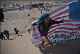  ?? RAMON ESPINOSA — THE ASSOCIATED PRESS ?? A migrant woman helps carry a handmade U.S. flag up the riverbank at the Mexico-U.S. border after getting past police at the border crossing in Tijuana, Mexico, on Sunday.