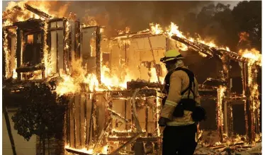  ??  ?? Unstoppabl­e: A fireman watches as flames consume this home in the Sonoma Valley