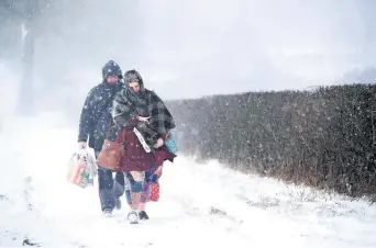  ??  ?? Una pareja camina en medio de una fuerte nevada después de haber tenido que abandonar su auto ante la acumulació­n de nieve en la localidad de Leek, en Inglaterra.