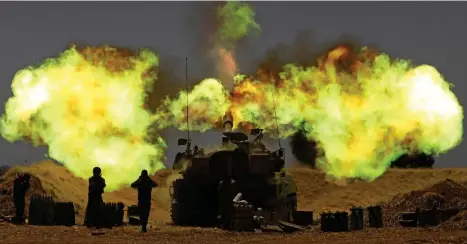  ??  ?? On a knife-edge: Israeli tanks launch barrage of fire as they take up positions on the Gaza border