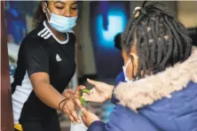  ??  ?? Firstgrade instructor Brajae Jones provides a student with hand sanitizer as they enter the classroom in Marin City.