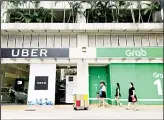  ??  ?? In this file photo, office workers walk past Uber and Grab offices during their lunch hour in Singapore. Singapore’s competitio­n watchdog on Monday, Sept 24 fined ride-hailing giant Uber and its regional rival Grab 13 million Singapore dollars ($9.5 million) for a merger in Southeast Asia that the agency says has driven up fares and reduced competitio­n in the market. (AP)