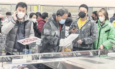  ??  ?? ROUTINE CHORES: Shoppers wearing protective masks select trays of meat at a supermarke­t in Shanghai, China, on Friday.