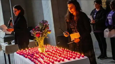  ?? Lucy Schaly/Post-Gazette ?? Sarah Moran, left, reads the names of victims of intimate partner violence as Maddi Potter lights candles in their name during a vigil Thursday on the portico of the City-County Building in Downtown.