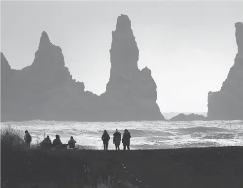  ?? FRANK AUGSTEIN / THE ASSOCIATED PRESS ?? People walk on the black sanded beach in Vik, Iceland, near the Volcano Katla. After decades of quiet, the volcano recently began rumbling. Its last eruption, in 1918, lasted almost a month, unleashed flood waters the size of the Amazon and extended...