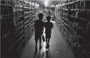  ?? KENT PORTER/PRESS DEMOCRAT VIA ASSOCIATED PRESS ?? Elijah Carter 11, left, and Robert Haralson, 12, help shop for their parents in a darkened Olivers Supermarke­t on Wednesday in Santa Rosa, Calif. The west side of the store was lit by patio lights powered by a generator as power was shut off again by Pacific Gas & Electric Co. due to high fire danger.