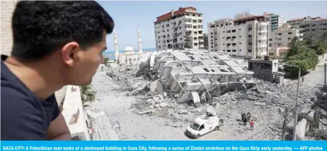  ?? — AFP photos ?? GAZA CITY: A Palestinia­n man looks at a destroyed building in Gaza City, following a series of Zionist airstrikes on the Gaza Strip early yesterday.