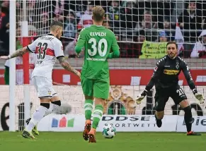  ?? FOTO: DPA ?? Stuttgarts Daniel Ginczek schießt das Tor zum 1:0. Mönchengla­dbachs Nico Elvedi und Torhüter Tobias Sippel können das nicht verhindern.