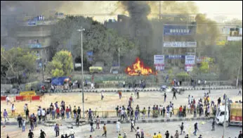  ?? MD MEHARBAN/HT PHOTO ?? A group of people along the road at Yamuna Vihar watch a vehicle on fire. 13 people have died and 253 were injured in the riots in north-east Delhi.