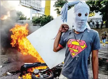  ?? FEDERICO PARRA/AFP ?? A hooded demonstrat­or stands near a burning motorbike in clashes with the riot police during an anti-government protest in Caracas, last week.