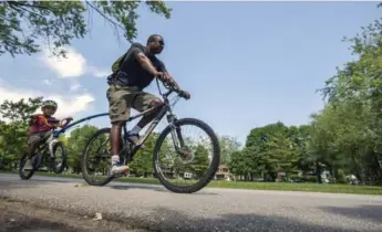  ?? MARCUS OLENIUK/TORONTO STAR ?? This father pulls his young son along behind him: a great way to prepare the child to ride his bicycle himself.