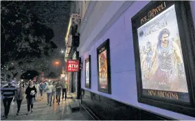  ??  ?? People walk past a poster of an Indian movie Baahubali: The Beginning
outside a movie theater in New Delhi, India.