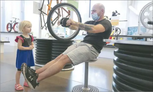  ?? (NWA Democrat-Gazette/Charlie Kaijo) ?? Brian Hess (center) of Fort Hood, Texas, uses a bicycle tire as a gyroscope while Eleanor Oliver, 2, (left) of Fayettevil­le watches at the Amazeum in Bentonvill­e.