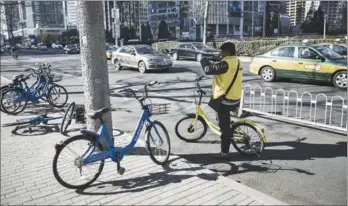  ?? SHEN QILAI / BLOOMBERG ?? An employee of Ofo Inc, a bike-sharing company, takes pictures of parked Bluegogo bikes in downtown Beijing. The proliferat­ion of bikesharin­g in the country has fuelled a new round of cash-guzzling competitio­n. With newcomers joining in the fray, most...