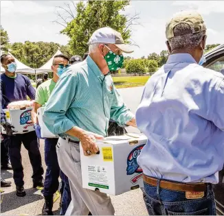  ?? JENNI GIRTMAN / FOR THE AJC ?? Georgia Agricultur­e Commission­er Gary Black (center) works alongside the DeKalb County fire rescue recruits and DeKalb CEO Michael Thurmond (right) to distribute fresh produce to DeKalb residents at James Hallford Stadium in Clarkston in May.