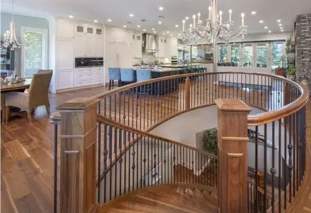  ??  ?? Engineered, walnut hardwoods sweep the main level at entry where a curved walnut staircase with wrought iron spindles flows elegantly to basement charms. The kitchen extends seamlessly into the front dining room and adjacent great room with views of the outdoor living space beyond.