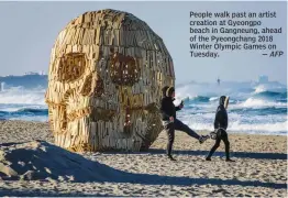  ?? — AFP ?? People walk past an artist creation at Gyeongpo beach in Gangneung, ahead of the Pyeongchan­g 2018 Winter Olympic Games on Tuesday.