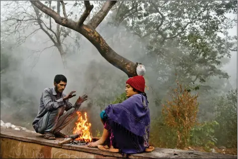  ??  ?? Two persons sit around a fire at a roadside on a cold foggy morning in New Delhi on Thursday. AFP