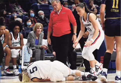  ?? Jessica Hill / Associated Press ?? UConn’s Paige Bueckers stumbles injured as Nika Mühl and coach Geno Auriemma looks on the second half against Notre Dame on Sunday in Storrs.