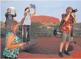  ??  ?? Tourists take photograph­s of the setting sun at Uluru.