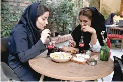  ?? AP Photo/Ebrahim Noroozi ?? ■ Two women drink Coca-Cola Wednesday at a cafe in downtown Tehran, Iran.