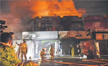  ??  ?? Bomberos voluntario­s tratan de controlar las llamas que se extendiero­n por algunos negocios de la calle Pettirossi.