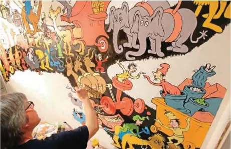  ??  ?? John Simpson, left, project director of exhibition­s for The Amazing World of Dr Seuss Museum, paints a mural based on artwork in the Dr Seuss book "Did I Ever Tell You How Lucky You Are?" on a wall at the museum, in Springfiel­d, Mass. — AP photos