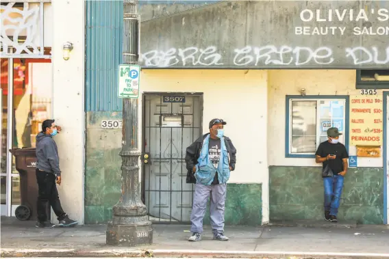  ?? Gabrielle Lurie / The Chronicle ?? People wait for the bus in the Fruitvale area of Oakland, where the infection rate is five times that in the wealthy suburbs of Alameda County.