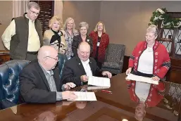  ??  ?? above Hempstead County Judge Haskell Morse, left, signs documents with Bruce Maloch, vice chairman of Farmers Bank & Trust, center, to conclude the purchase of the bank building to be used as a courthouse. Patricia J. Harris, far right, directs the...