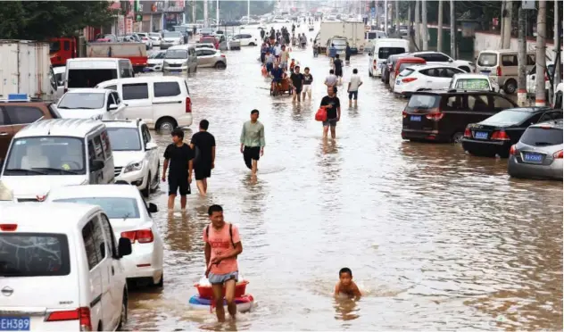  ?? Reuters ?? ↑
People wade through floodwater­s following a heavy rainfall in Zhengzhou on Friday.