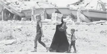  ??  ?? Displaced Iraqi residents carry boxes of biscuits given by an aid organisati­on during the first day of Aidilfitri celebratio­n in West Mosul. — Reuters photo