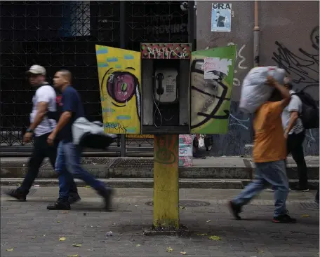  ?? AP FILE ?? FOR SALE: Pedestrian­s walk past an out-of-service National Telephone Company of Venezuela, CANTV, phone booth, in Caracas, Venezuela, on Friday. A number of Venezuelan state-owned companies, including in the telecommun­ications sector, will sell up to 10% of their shares starting Monday.