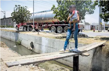  ?? JOSEFINA VILLARREAL ?? Ante la destrucció­n de los puentes, los habitantes del barrio instalaron ayer estas improvisad­as tablas para poder pasar por el canal del Corredor Portuario. Una mujer cruza con su bebé en brazos.