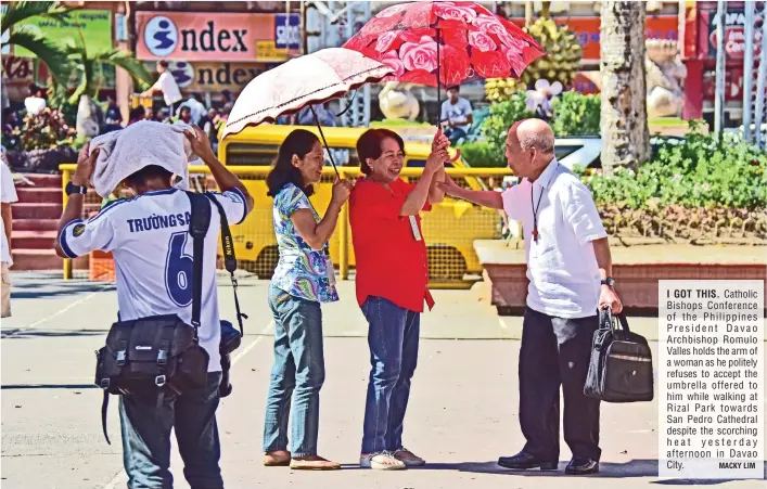  ?? MACKY LIM ?? I GOT THIS. Catholic Bishops Conference of the Philippine­s President Davao Archbishop Romulo Valles holds the arm of a woman as he politely refuses to accept the umbrella offered to him while walking at Rizal Park towards San Pedro Cathedral despite...