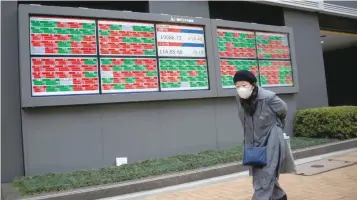  ?? — Reuters ?? A woman walks past electronic boards showing stock prices outside a brokerage in Tokyo.