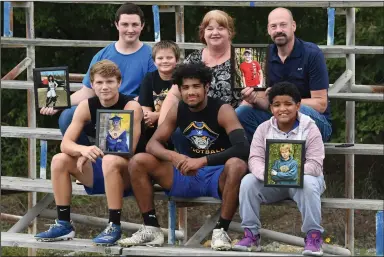  ?? (NWA Democrat-Gazette/J.T. Wampler) ?? Cedarville junior Darryl Kattich, front row second from left, sits with his parents and five of his nine siblings and parents Angie and Mark Kattich, top right. The rest of the Kattich family includes front row, from left, Bruce Turney, holding a photo of Jacob Kattich, Darryl Kattich and Dakota Kattich, holding a photo of Matthew Kattich. Top row, Jonathan Kattich, holding a photo of Chanel Kattich, Grayson Kattich, Angie and Mark, who is holding a photo of Wyatt Kattich.