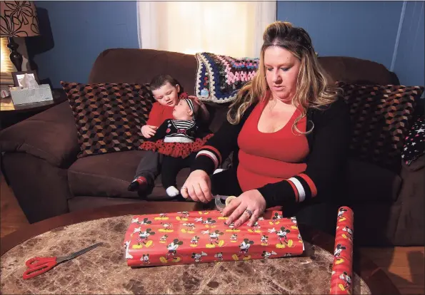  ?? Christian Abraham / Hearst Connecticu­t Media ?? Michelle Doheny- Meeker wraps a present at her home in Derby on Thursday. At left is her children Camden Meeker, 5, and Autumn Meeker, 5 months. Michelle, who has been laid off during the pandemic, is trying to earn money by wrapping, hiding and shopping for Christmas gifts for other moms.