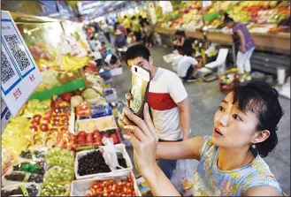  ??  ?? This photo taken on June 27, shows a woman making purchases by scanning QR codes using her smartphone at a fruit stall in a market in Beijing. China was the first country in the world to use paper money but centuries later the
soaring popularity of...