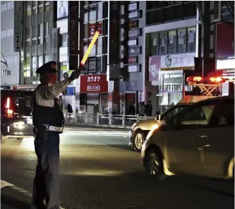  ?? The Yomiuri Shimbun ?? A police officer directs traffic just after midnight on March 17 at an intersecti­on in Taito Ward, Tokyo, during a power outage caused by an earthquake.